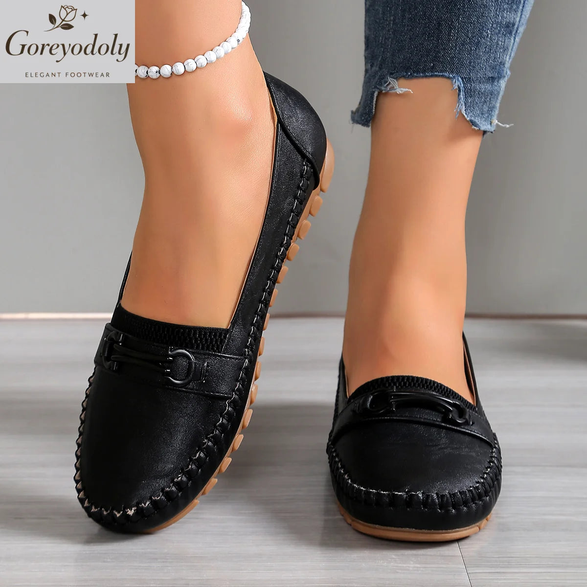 Vue de face de deux mocassins noirs à enfiler avec ornement métallique et surpiqûres apparentes, portés avec un jean